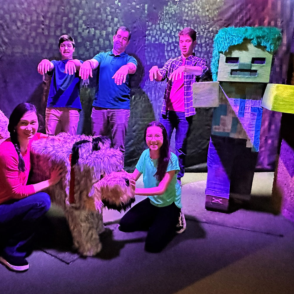 Group of people posing with life sized Wolf mob and green Zombie mob sculptures.